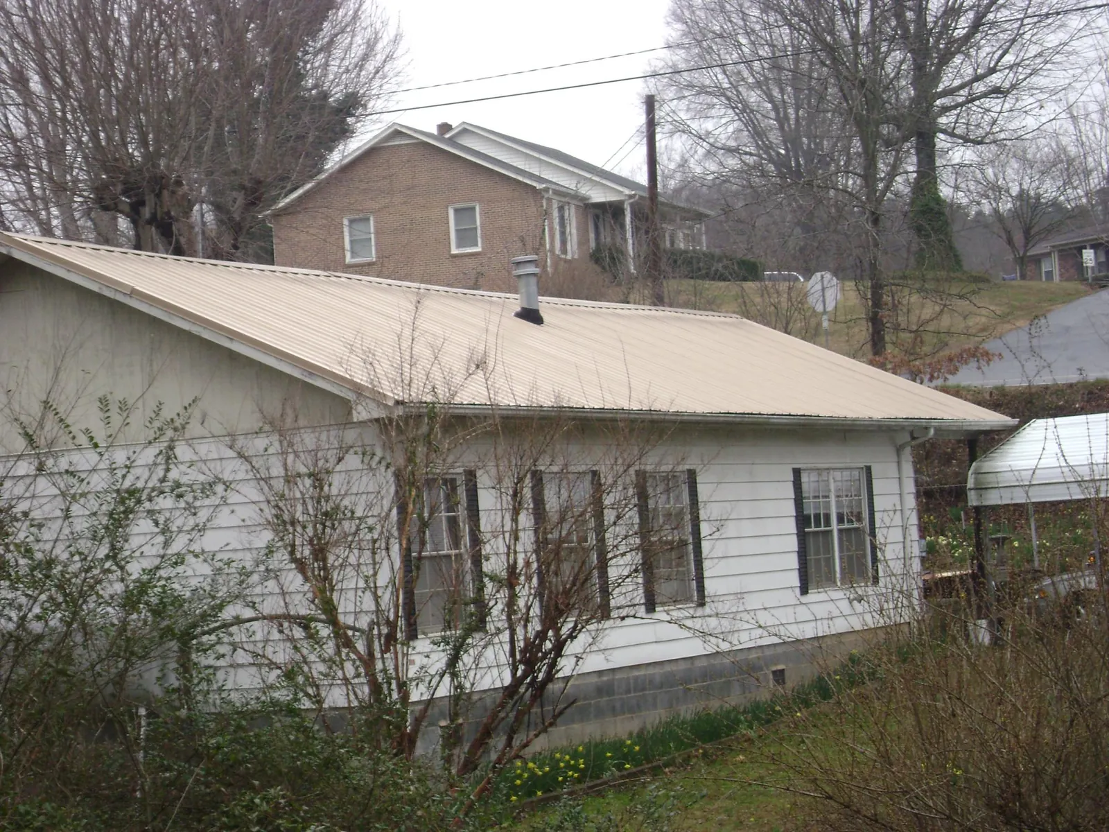 Tan metal roof on a white sided house set into a hillside — Commercial Roofing by Roofing Brothers in Jackson